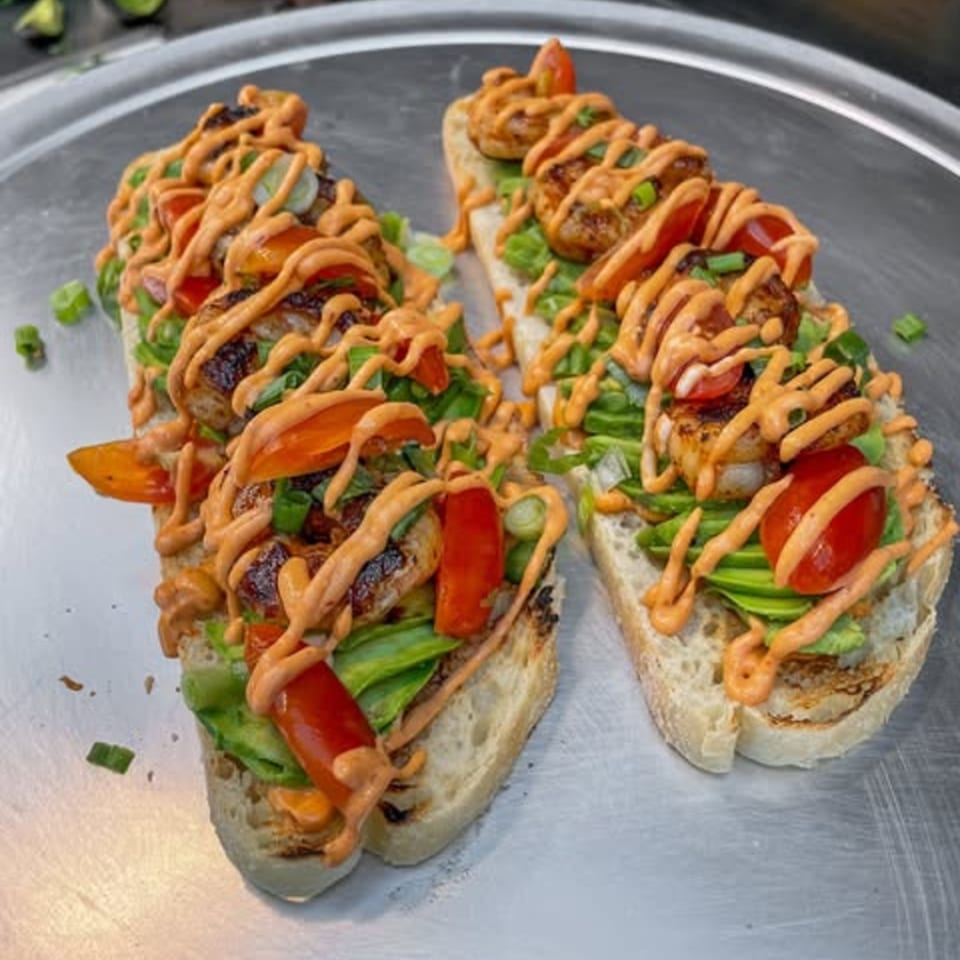 Two shrimp and avocado toasts with red peppers, green onions, and orange sauce on a metal tray.