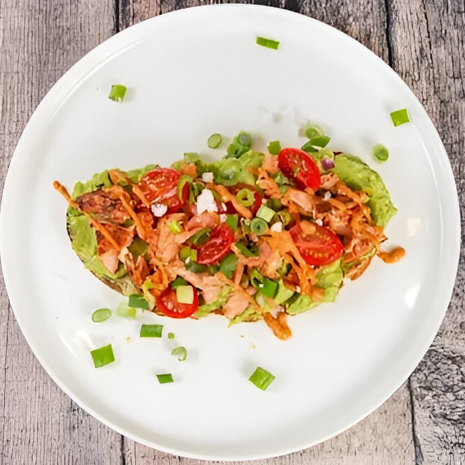 A Lo Fresco's healthy avocado boat with salmon, tomatoes, and green onions on a white plate.