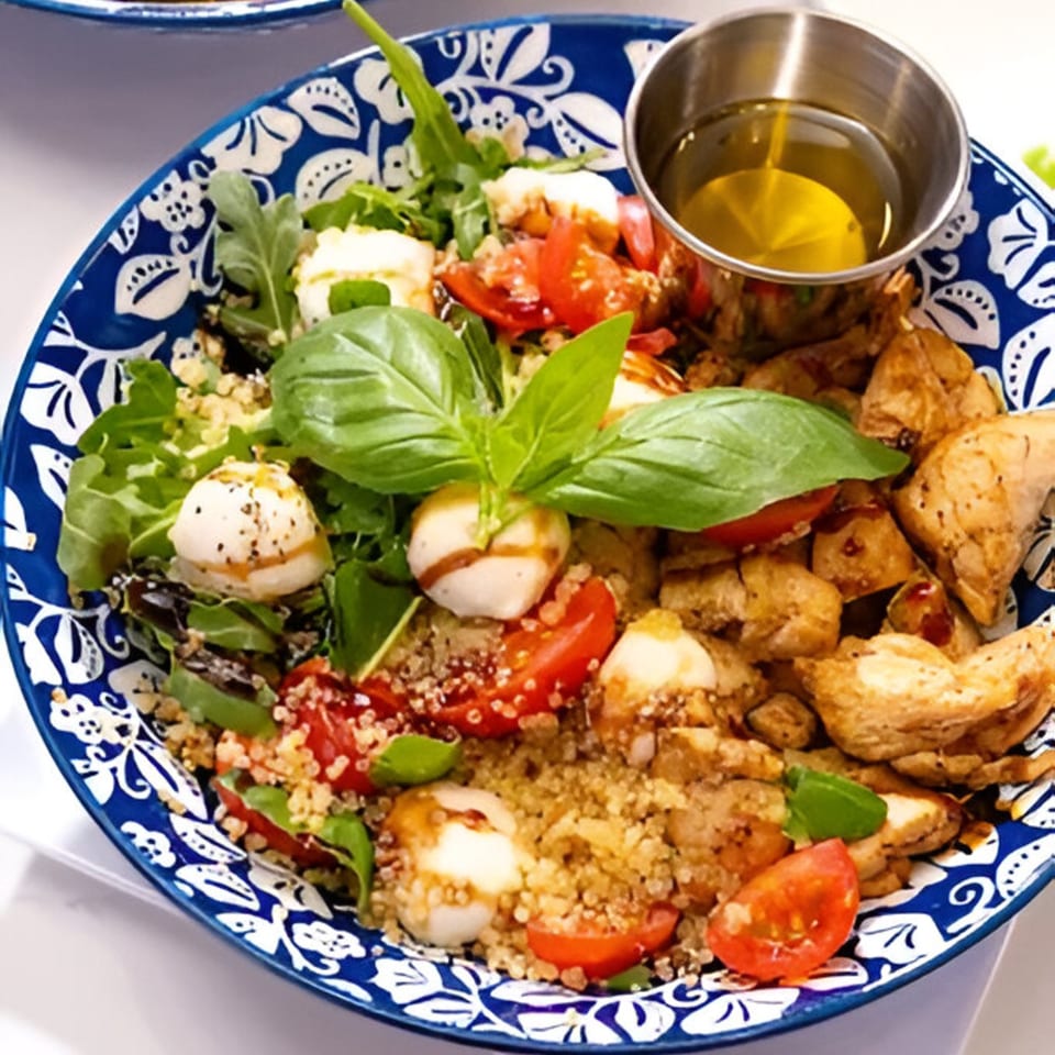 A Lo Fresco's healthy quinoa salad with chicken, tomatoes, mozzarella, and basil in a blue patterned bowl.