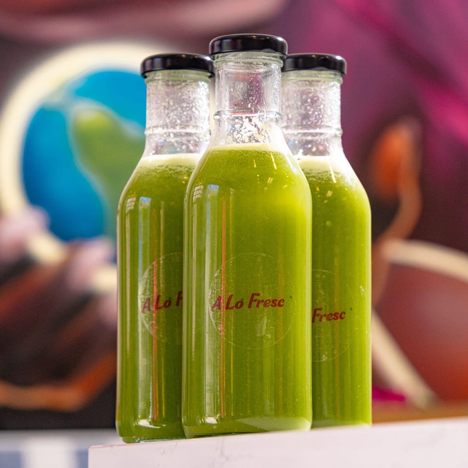 Three bottles of A Lo Fresco green juice with black caps on a white surface.