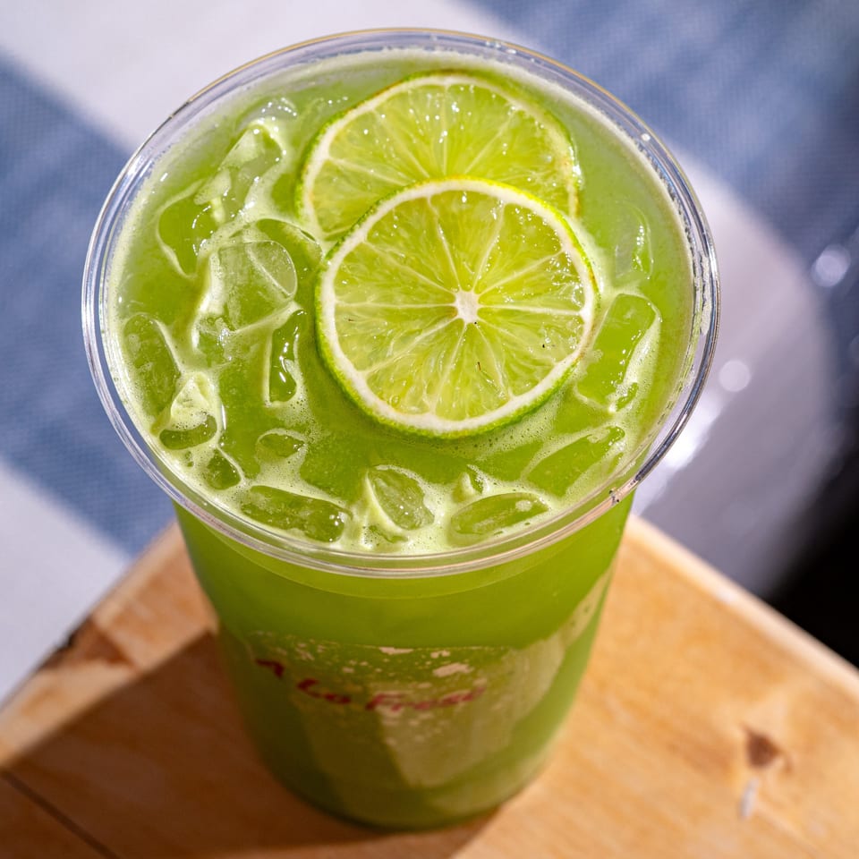 A Lo Fresco's vibrant green drink with ice and two lime slices, on a wooden surface.