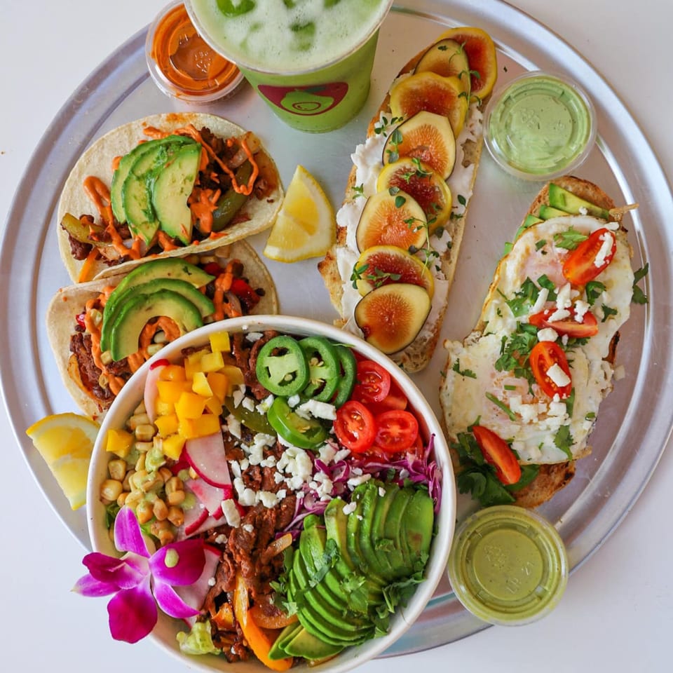 A Lo Fresco's healthy spread: tacos, fig toast, egg toast, and a colorful salad bowl with green juice.