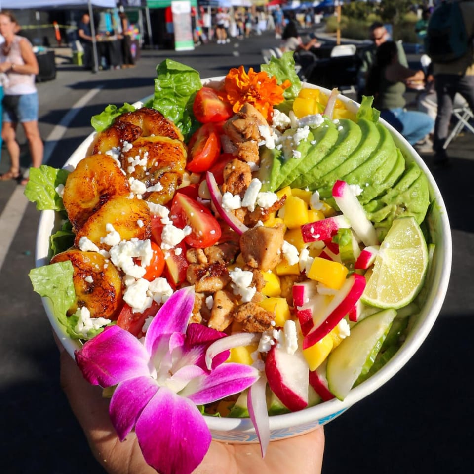 A Lo Fresco's healthy salad with plantains, chicken, avocado, mango, and feta, garnished with an orchid.